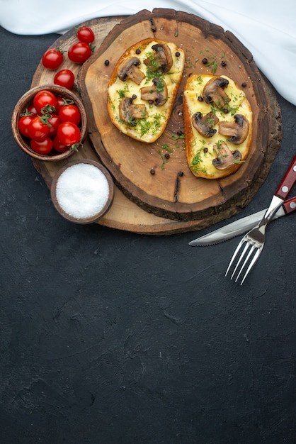 Above view of tasty snack with mushrooms tomatoes salt on wooden board on black background