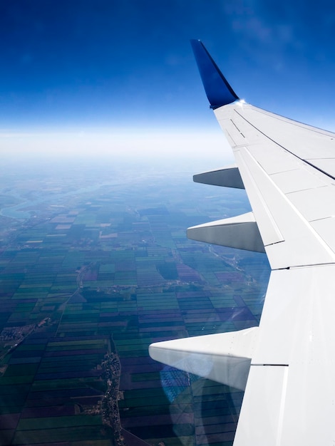 Фото Вид через иллюминатор самолета с возделываемыми полями, голубым небом, светлыми облаками и частью самолета