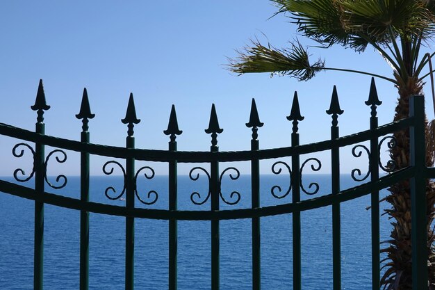 Photo view through black sharp fencing to azure sea water surface till skyline on heat sunny day