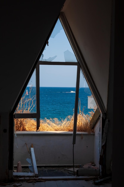 View through a broken window to the sea and the beach with palm trees on a sunny summer day Poor life concept overlooking the rich