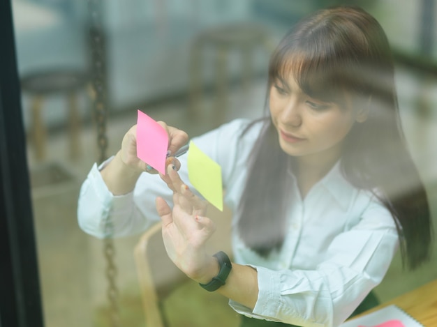 view through glass business female attaching sticky note planning strategy on colourful papers