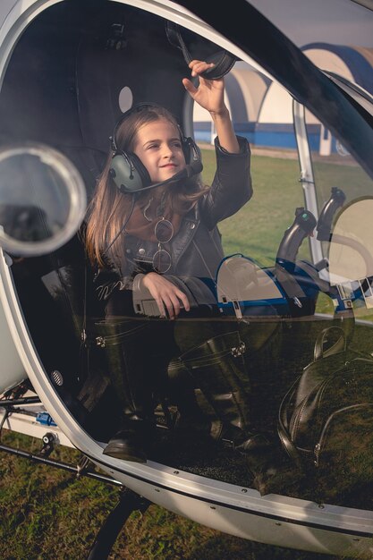 View through glass of preteen girl in headset sitting in helicopter cockpit