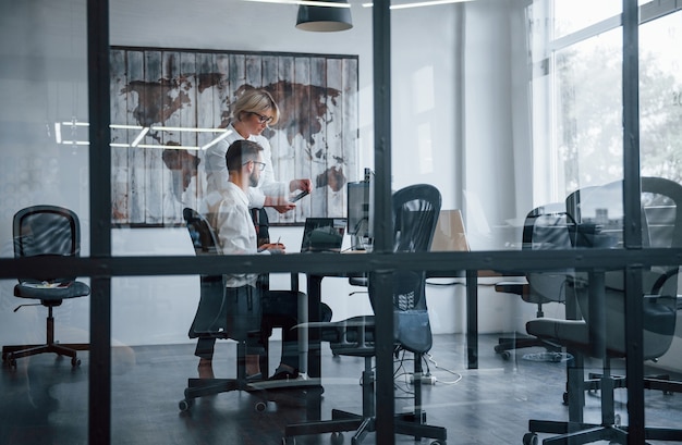 View through the glass. Two stockbrokers in formal clothes works in the office with financial market.