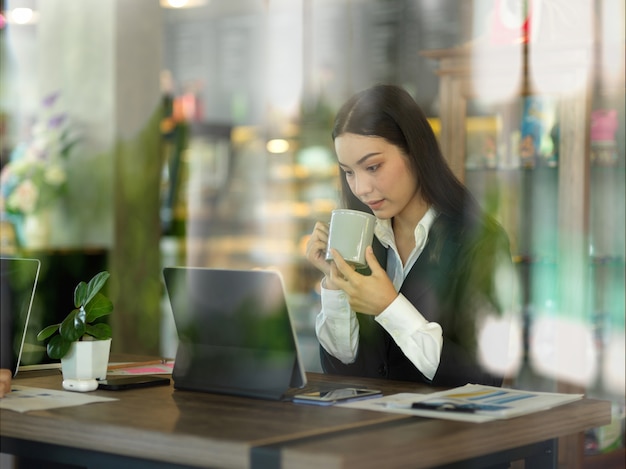 実業家のガラスの壁を通して見るカフェでタブレットを操作しながらコーヒーブレイク