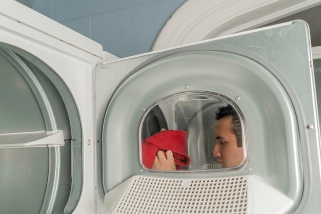 View through the washing machine door of a laundry person putting red clothes inside for washing