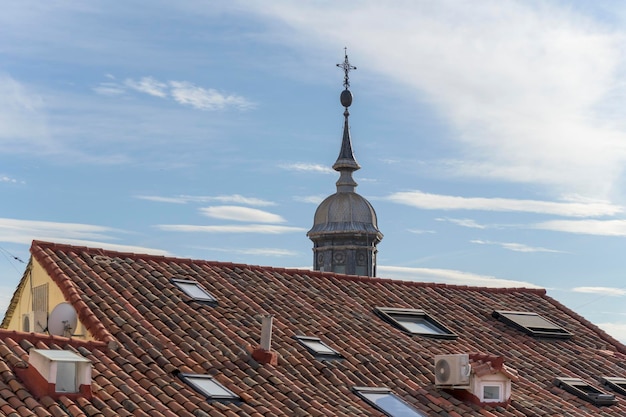 View of the tiles of a vintage roof with skylights and a dome in the background