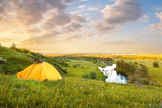 view of tourist tent on green meadow at sunrise or sunset
