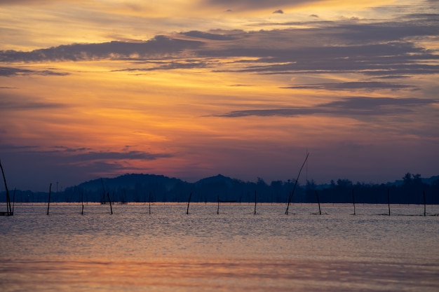 View of twilight sky reflected on water surface in Songkhla Lake, with mountains in backgr