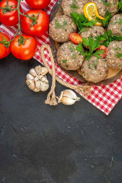 Above view of uncooked meatballs on a wooden cutting board and fresh vegetables green on dark background