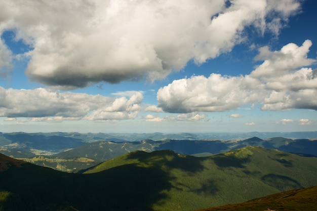 Вид на долину с вершины горы на фоне нескольких лесистых гор и небо с облаками