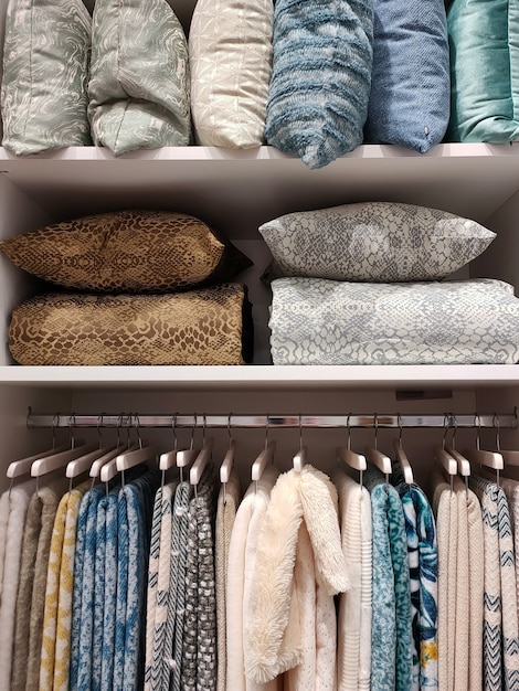 View of a wardrobe with woolen blankets hanging on hangers and pillows and blankets on the shelves.