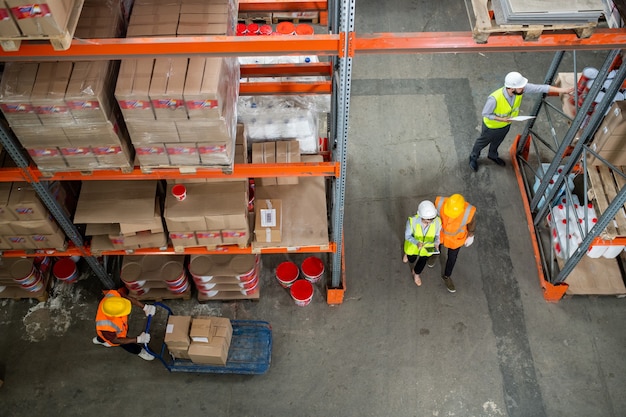 Above view of warehouse staff in hardhats and reflective vests working with boxes and sorting it on shelves