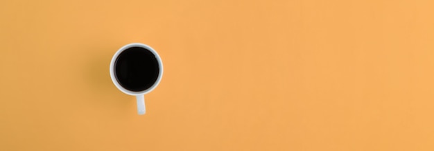 above view white cup with coffee on orange background with copy space.