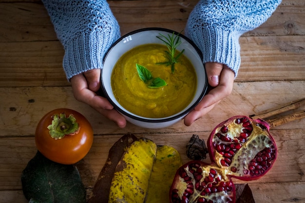 Above view of woman hands holding warm healthy autumn winter soup food to have lunch alone. Pommegranate and vegetables diet nutrition concept. wooden rustic table. Health people lifestyle