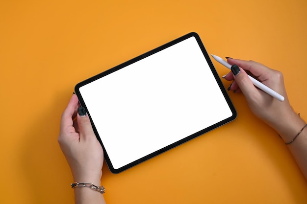 Above view woman holding mockup digital tablet and stylus pen on yellow background