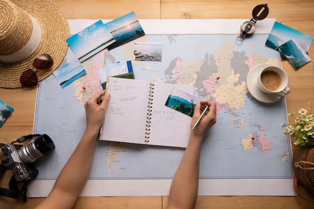 Above view of woman sitting at table with world map and making notes about sights