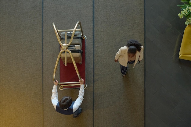 Above view of young black woman passing by bellboy pushing cart