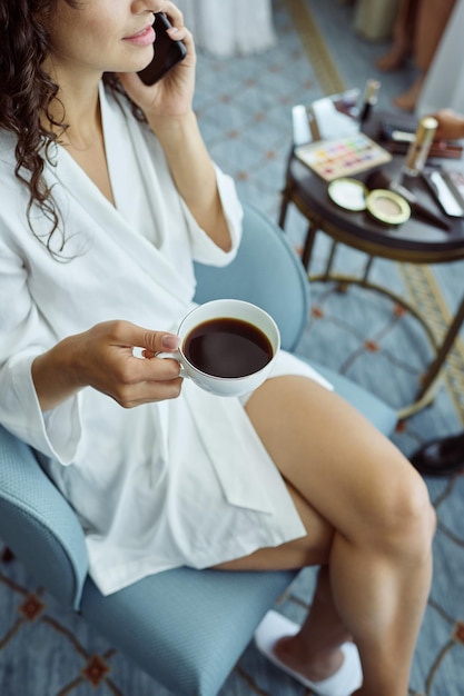 Sopra la vista della giovane sposa con una tazza di americano che parla al cellulare