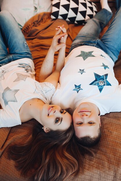 Above view of young couple laying together in bed at studio Two people smiling and holding hand spending time together and having fun wearing in white tshirt Concept of love and relationship