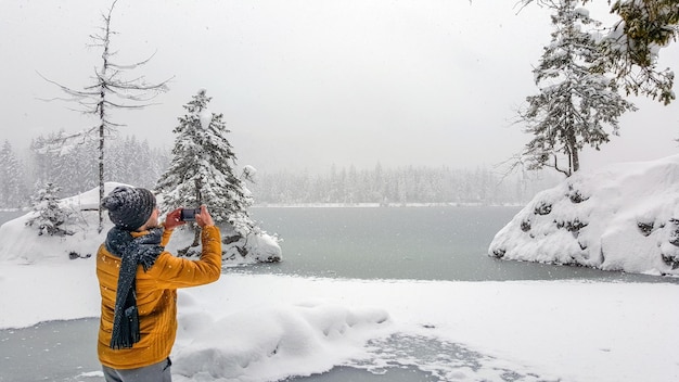 Foto vista di un giovane maschio che scatta una foto di un lago ghiacciato