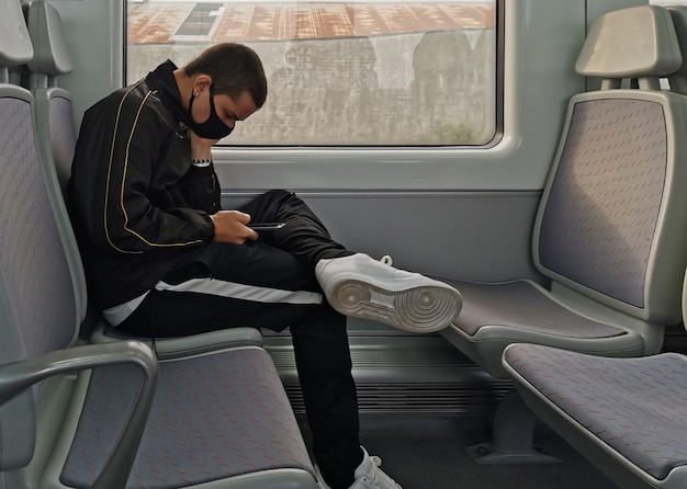 Photo view of young man sitting alone on train seat wearing mask