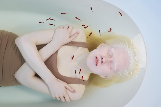 Above view of young pale woman with albinism lying in clear water