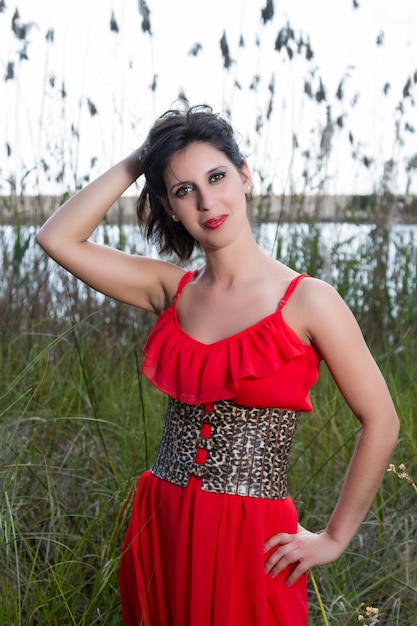 View of a young woman in a red dress surrounded by tall plants in a marshland.