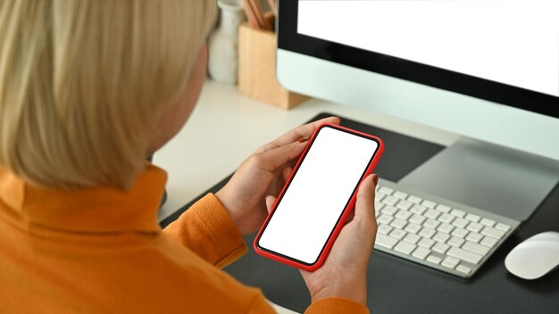 View over young woman shoulder holding mobile phone while sitting in front of computer in office