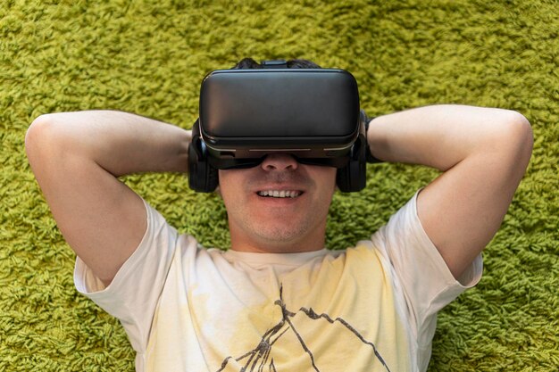 Photo viewing 360 videos young caucasian man lie on a floor in a living room with vr glasses with smile on his face