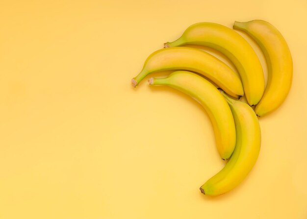 Vijf bananen liggen op een gele achtergrond in een hoek en laten ruimte voor tekst