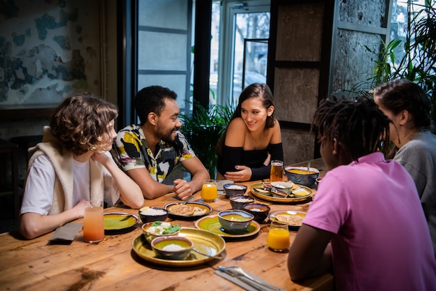 Vijf glimlachende studenten die een snack hebben en in universiteitskantine babbelen