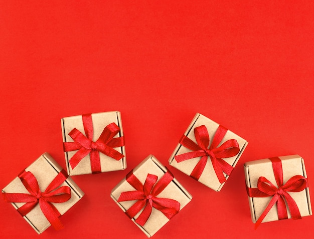 Vijf kleine bruine cadeautjes met een rood lintje op een rode achtergrond