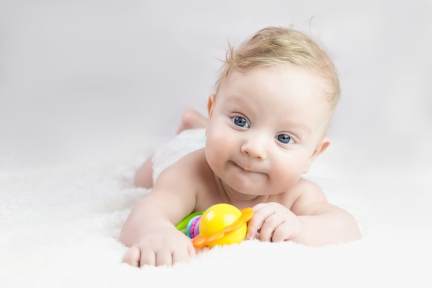 Vijf maanden oude blonde jongen met blauwe ogen ligt op zijn buik met een speeltje in zijn handen