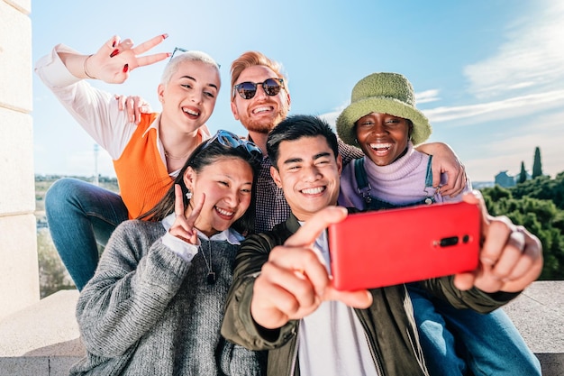 Vijf multiraciale vrienden die een foto maken met een mobiele telefoon die voor de camera poseert en glimlacht