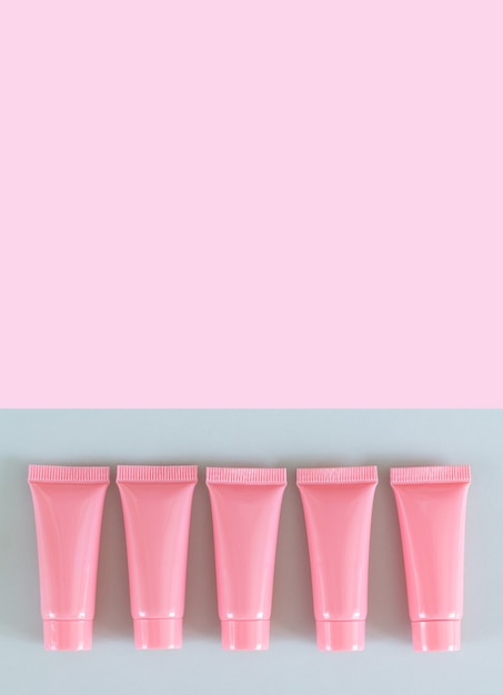 Vijf roze cosmetische containers bovenaanzicht op grijze achtergrond. Kuuroordproductbuizen of flessen met exemplaarruimte