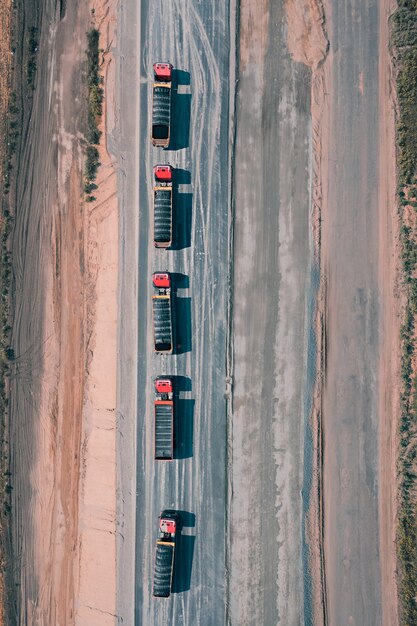 Vijf vrachtwagens met vracht rijden over een asfaltweg in het midden van een drone-opname vanuit de woestijn