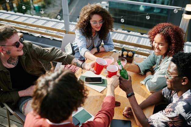 Vijf vrolijke jeugdvrienden rammelend met hun drankjes boven tafel in café