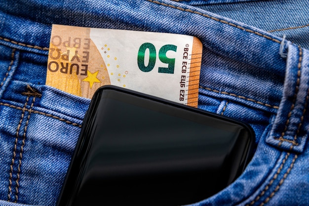 Vijftig euro-bankbiljet en smartphone in jeanszak. geld voor reizen en winkelen