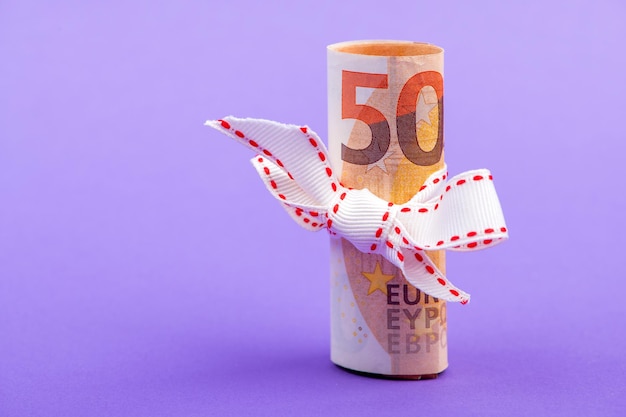 Foto vijftig euro bankbiljet geld rol gebonden met een wit cadeau lint geïsoleerd op een paarse achtergrond