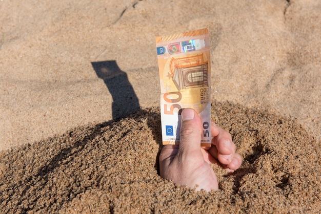 Vijftig euro in de hand van een man die uit het zand steekt