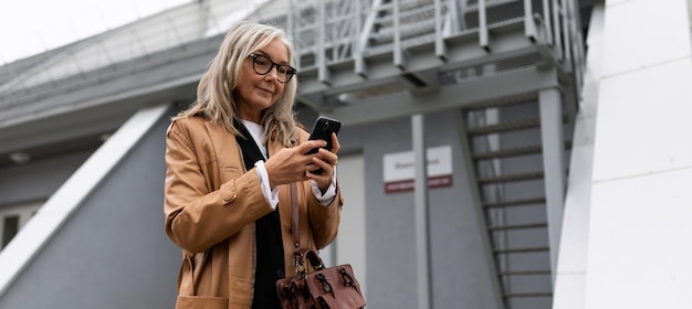 Vijftigjarige zakenvrouw met een mobiele telefoon in haar handen tegen de achtergrond van een industrial