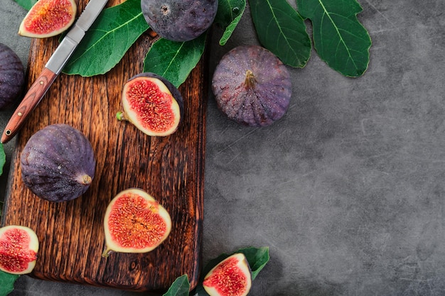 Vijgen in plakjes gesneden op een houten snijplank naast een oud mes Vijgen omgeven door vijgenboombladeren op grijze keukentafel seizoensgebonden rijp fruit mediterraan dieetidee voor achtergrond