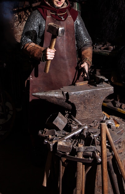 写真 バイキングは鍛冶屋で武器と剣を鍛造します。戦士の服を着た男が鍛冶場にいます。