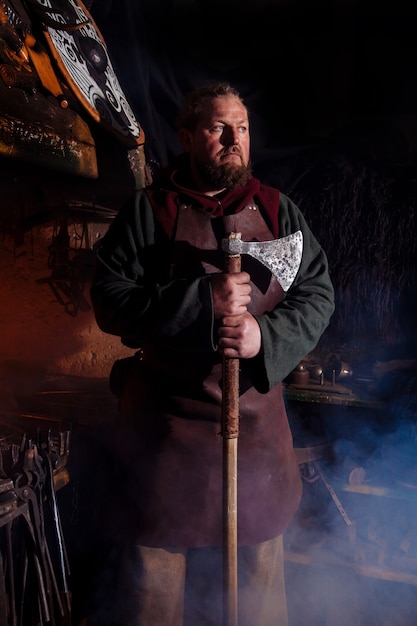 Viking forges weapons and swords in the smithy. A man in a warrior's clothes is in the smithy.