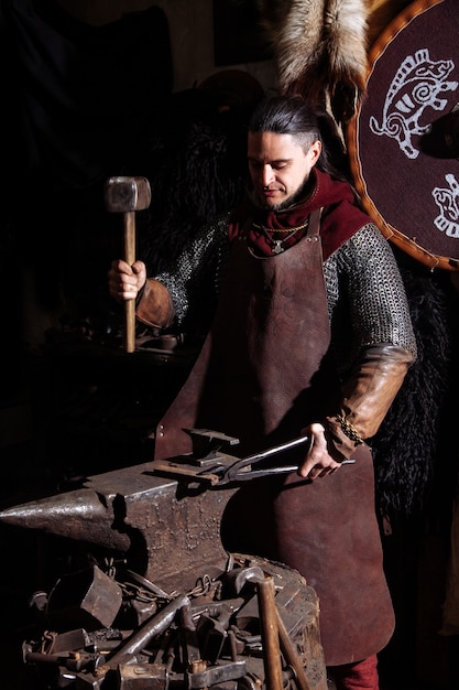 バイキングは鍛冶屋で武器と剣を鍛造します。戦士の服を着た男が鍛冶場にいます。