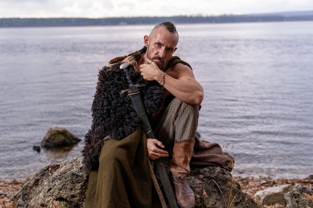 viking is thoughtful and sits on a stone holding a sword inserted into a sheath