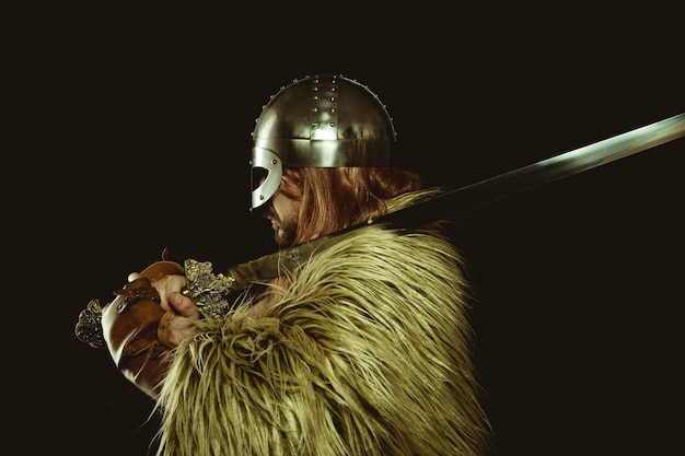 Viking warrior with metallic helmet and animal skins. leather\
gauntlets, red wooden shield with gold decorations and steel\
sword