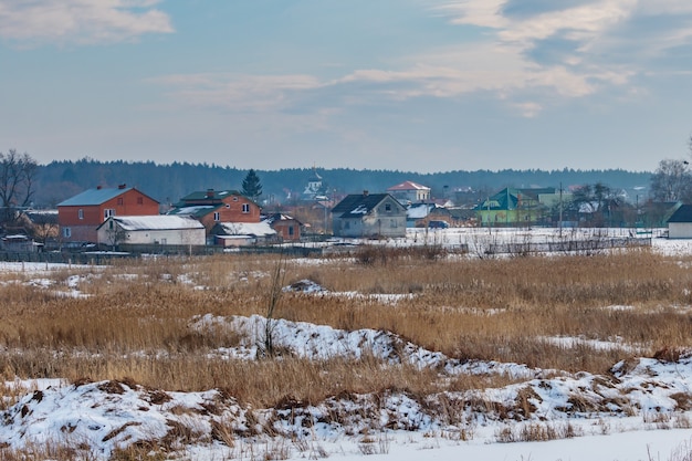 Village houses at winter day against snowy farm field