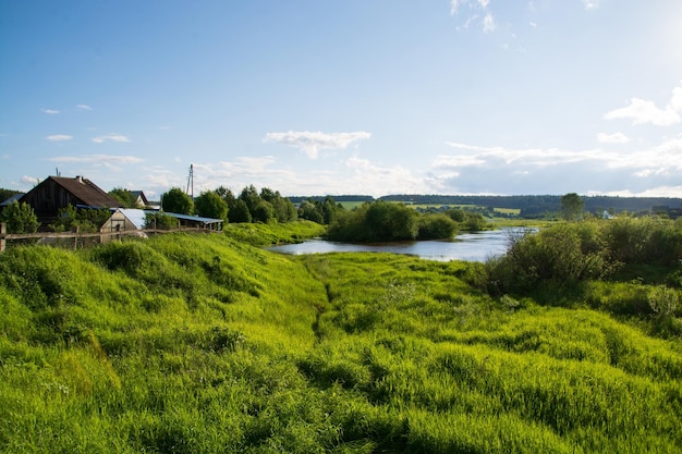 Un villaggio sulla sponda del fiume con erba verde brillante e un bel cielo