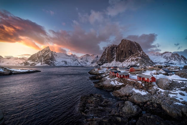 Lofoten 섬, 노르웨이에서 일몰에 눈이 덮여 백그라운드에서 산들과 바다로 붉은 통나무 집